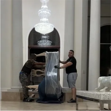 Two Miami Moving Company movers carrying a wrapped piece through a marble lobby